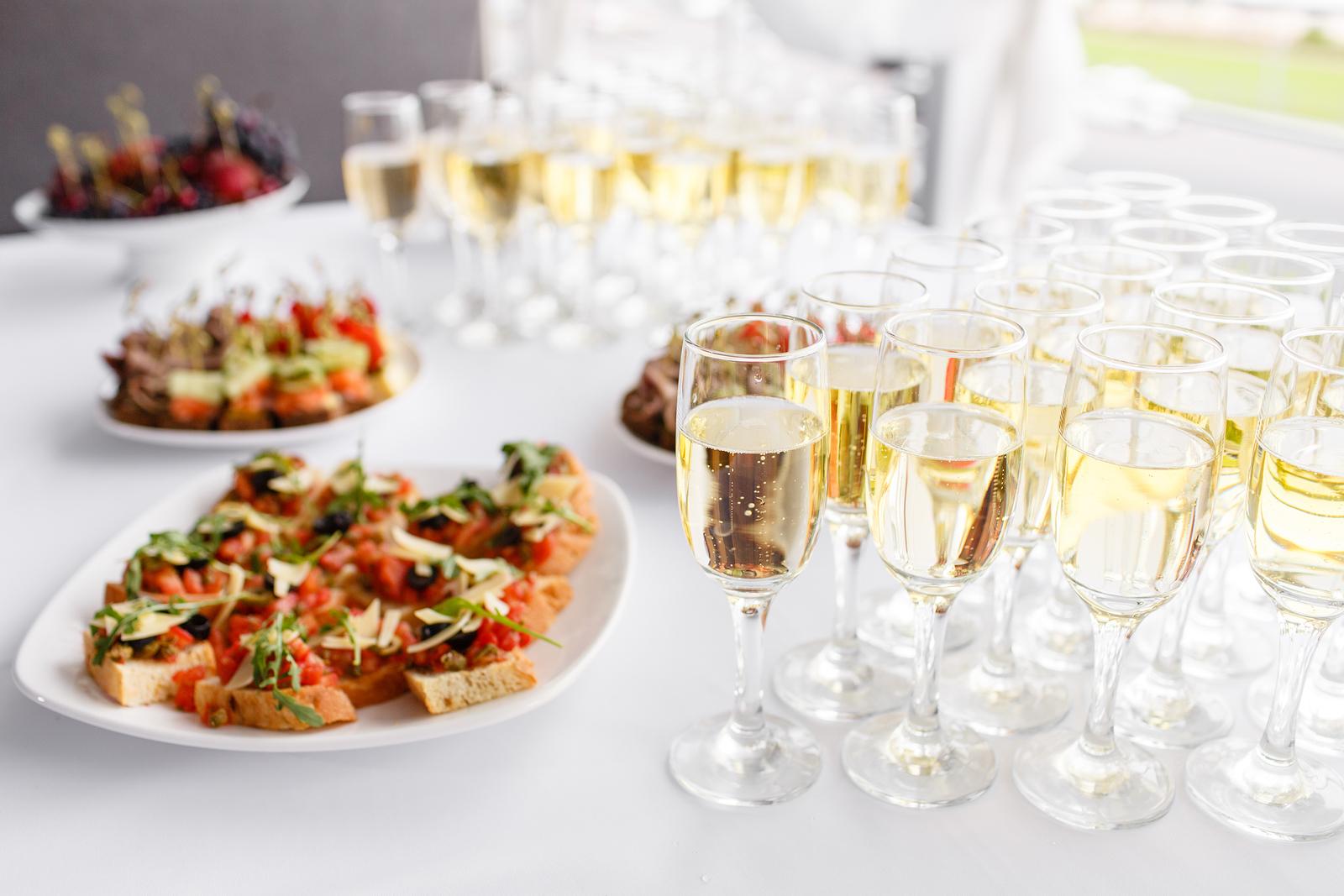 恭贺新禧. 餐厅的桌子上有很多玻璃杯、香槟或葡萄酒. 自助餐桌上有很多美味的小吃. 小点心，意式烤面包和小甜点放在木板上